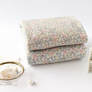 May include: Two pieces of white fabric with a floral print in shades of pink, yellow, and grey. The fabric is folded and stacked on a white surface.