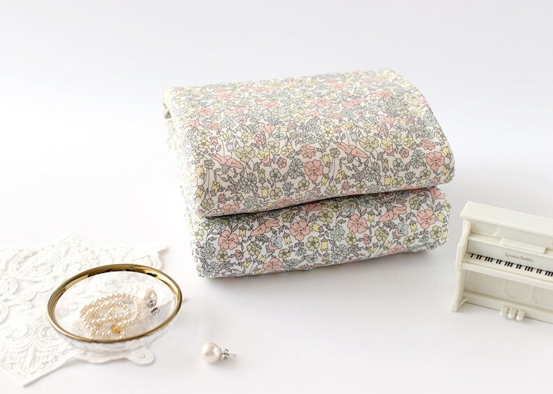 May include: Two pieces of white fabric with a floral print in shades of pink, yellow, and grey. The fabric is folded and stacked on a white surface.