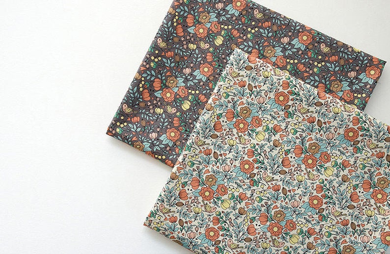 May include: Two fabric squares with a floral pattern. One square is a dark gray background with orange, yellow, and blue flowers. The other square is a light cream background with orange, yellow, and blue flowers.