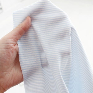 May include: Close-up of a light blue and white striped fabric. The fabric is soft and has a subtle texture.