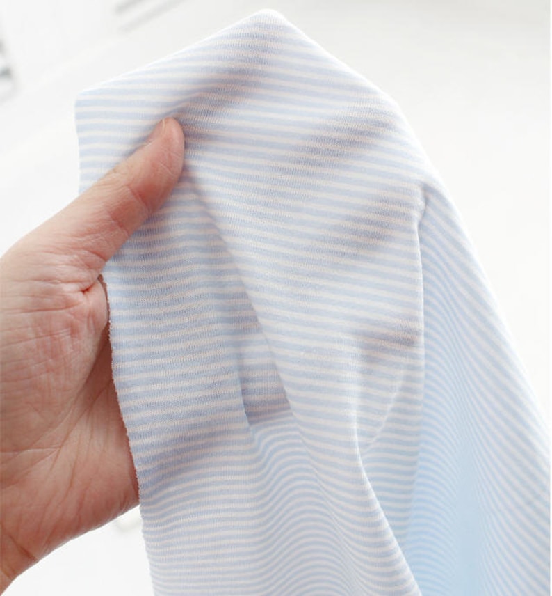 May include: Close-up of a light blue and white striped fabric. The fabric is soft and has a subtle texture.