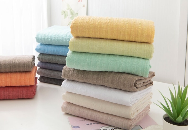 May include: A stack of ten fabric swatches in various colors, including light blue, yellow, green, brown, white, and pink. The swatches are folded and stacked on a white surface.