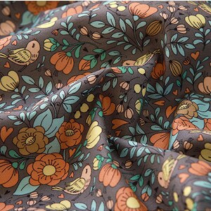 May include: A brown fabric with a repeating pattern of orange flowers, green leaves, and small birds. The fabric has a vintage feel and would be perfect for crafting projects.