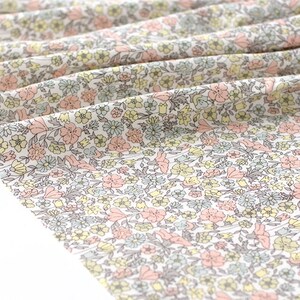 May include: White fabric with a small-scale floral print in shades of pink, yellow, and blue. The fabric is folded and has a soft, crinkled texture.