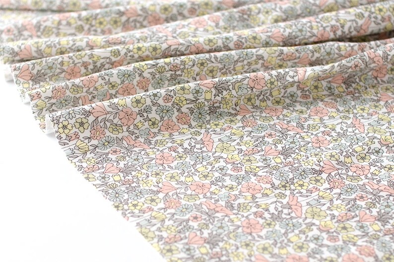 May include: White fabric with a small-scale floral print in shades of pink, yellow, and blue. The fabric is folded and has a soft, crinkled texture.