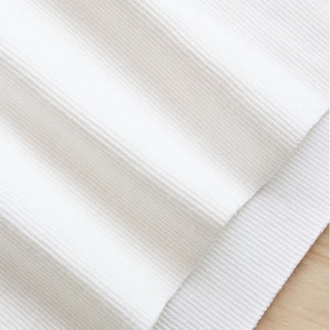 May include: White ribbed fabric with a smooth texture. The fabric is folded in half, showing the inside of the fabric.