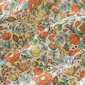 May include: A cream-colored fabric with a repeating pattern of orange and yellow flowers, green leaves, and small birds. The pattern is whimsical and charming.