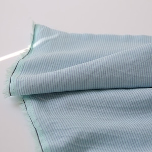 May include: A light blue fabric with thin white stripes. The fabric is folded and has a raw edge.