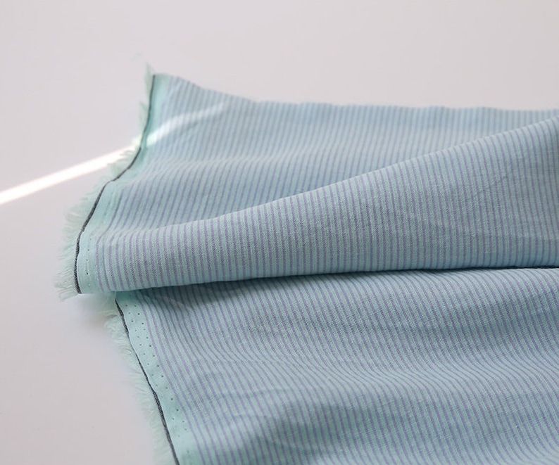 May include: A light blue fabric with thin white stripes. The fabric is folded and has a raw edge.