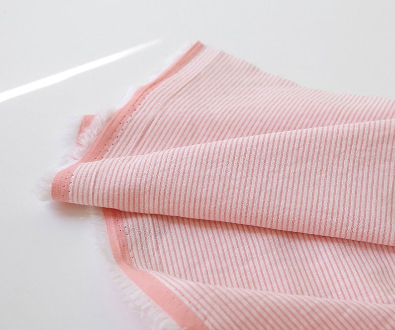 May include: Pink and white striped fabric with a pink border. The fabric has a soft, textured feel.