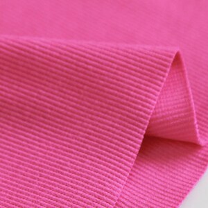 May include: Close-up of a bright pink ribbed fabric. The fabric is folded over, showing the texture of the ribbing.