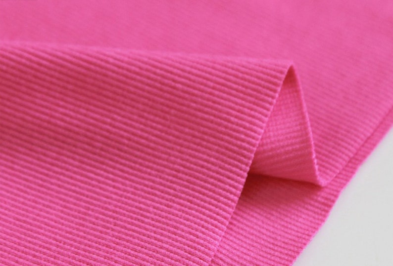 May include: Close-up of a bright pink ribbed fabric. The fabric is folded over, showing the texture of the ribbing.