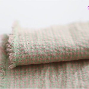 Pu&ograve; includere: Tessuto a quadri verde e rosa con un bordo sfrangiato. Il tessuto &egrave; piegato a met&agrave;.