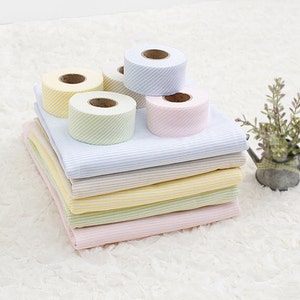 May include: A stack of striped fabric in pink, green, yellow, and beige with four rolls of striped ribbon in yellow, light blue, and pink.