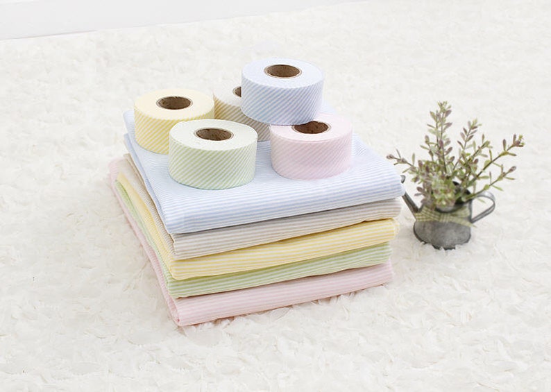 May include: A stack of striped fabric in pink, green, yellow, and beige with four rolls of striped ribbon in yellow, light blue, and pink.