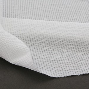 May include: White waffle-weave fabric with a fine, textured pattern. The fabric is folded and draped over a dark surface.