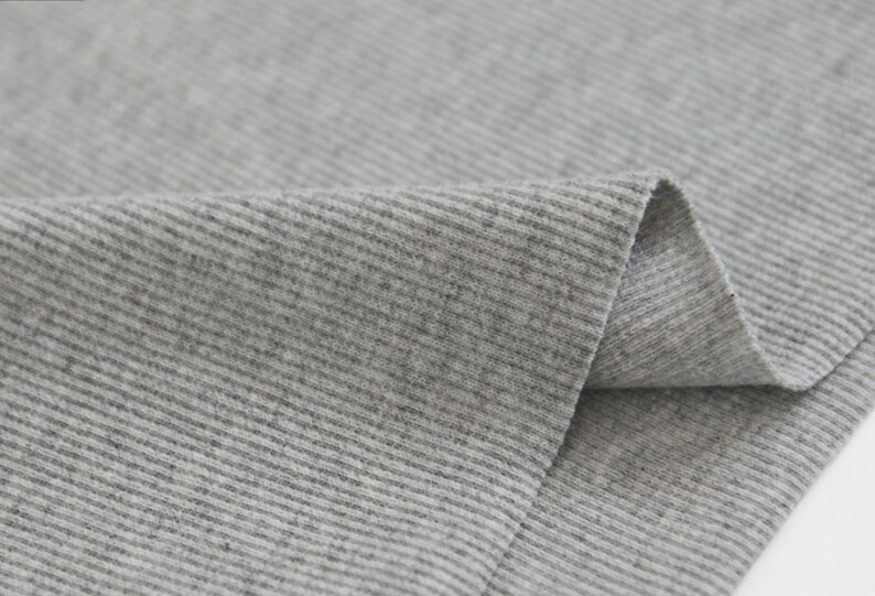 May include: Close-up of a gray ribbed fabric. The fabric is soft and has a subtle texture.