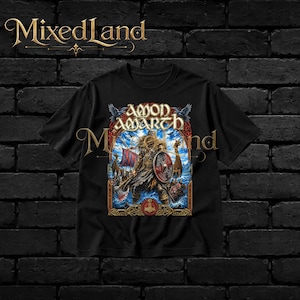 Könnte beinhalten: Ein schwarzes Kurzarm-T-Shirt mit einem Grafikdruck eines Wikingerkriegers, der einen Schild und eine Axt hält, mit dem Text Amon Amarth darüber. Das Design zeigt ein Langschiff auf blauer See, umrahmt von einer verzierten goldenen Bordüre.