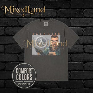 Puede incluir: Una camiseta de manga corta en color gris carbón con un estampado gráfico del personaje del videojuego Half-Life, Gordon Freeman, con gafas y perilla, junto al logotipo de Half-Life. Incluye una etiqueta de Comfort Colors Pepper.