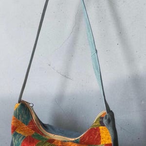 May include: A hobo-style shoulder bag featuring a patchwork pattern of rectangular blocks in red, orange, yellow, and green with etched line details. The bag has solid gray side panels, a matching gray shoulder strap, and a top zipper closure.