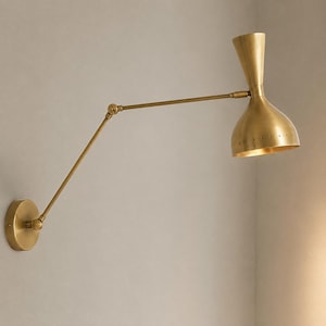 May include: A brass wall lamp featuring an adjustable swing arm with two pivot points and a conical shade. The shade has a series of small perforations along the lower edge, and the entire fixture is finished in a polished metallic gold tone.