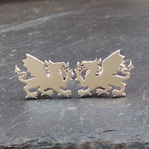 May include: A pair of silver dragon cufflinks. The dragons are facing each other with their wings spread out.
