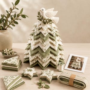 以下が含まれることがあります： 緑と白の模様の葉を重ねた布製のクリスマスツリーの彫刻で、頂上には白い鳩の置物が飾られています。セットには、三角形や星型の布パーツの山、糸巻き、布製のリボンが含まれています。