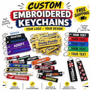 May include: A collection of rectangular embroidered keychains in various colors including black, white, blue, red, green, yellow, and purple. Each keychain features a metal ring and displays diverse text, logos, and graphic designs.
