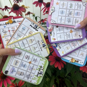 May include: A collection of rectangular bingo cards featuring various themes including Mickey and Friends, Pin Bingo, Princess Bingo, and Villain Bingo. Each card is accented with a small enamel pin shaped like a bottle or character icon.