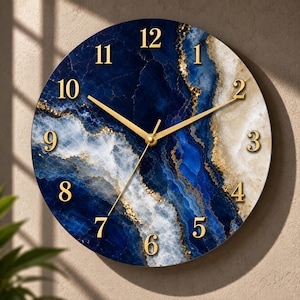 May include: A round wall clock featuring a deep blue and white marble-like pattern with gold-coloured veins. The clock face displays raised gold-coloured Arabic numerals from one to twelve and three thin gold-coloured hands at the centre.