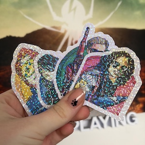 May include: A set of four die-cut stickers featuring illustrated characters with a holographic finish. The stickers display colourful, detailed portraits of individuals with varied hairstyles and clothing, all rendered in a comic book art style.