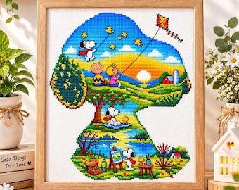 May include: A framed cross-stitch embroidery featuring a Snoopy-shaped silhouette filled with a colourful landscape. The scene depicts Snoopy and Charlie Brown flying a kite, Snoopy painting at an easel, and Woodstock characters in a vibrant outdoor setting with a blue sky, green hills, and a sunset.