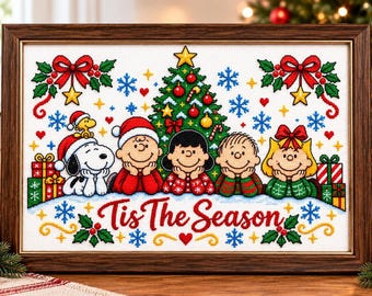May include: A framed cross-stitch embroidery featuring Snoopy, Woodstock, and the Peanuts gang in front of a decorated Christmas tree. The text Tis The Season is stitched in red at the bottom, surrounded by snowflakes, holly, and gift boxes.