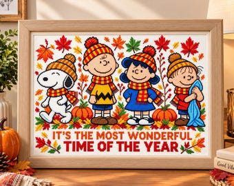 May include: A framed cross-stitch embroidery featuring Snoopy, Charlie Brown, Lucy, and Linus wearing autumn hats and scarves, surrounded by colourful fall leaves and pumpkins, with the text IT'S THE MOST WONDERFUL TIME OF THE YEAR.