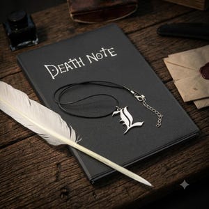 Puede incluir: Un cuaderno negro con el texto blanco Death Note impreso en la portada, que incluye un colgante plateado con forma de letra L en un collar de cordón negro y una pluma blanca de ave colocada en diagonal sobre la superficie del cuaderno.