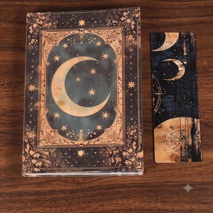 May include: A rectangular hardcover book featuring a dark blue and gold celestial cover design with a large crescent moon and stars, accompanied by a matching vertical bookmark displaying moon phases and a circular compass-like graphic element.