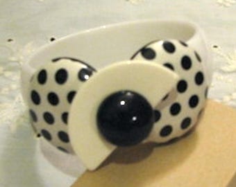 May include: White bangle bracelet with a black and white polka dot design and a large black circle in the center.