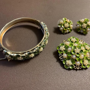 May include: A vintage jewelry set featuring a hinged bangle bracelet, a pair of stud earrings, and a brooch. The pieces are gold-toned with green enamel and faux pearl accents. The bracelet has a safety chain.
