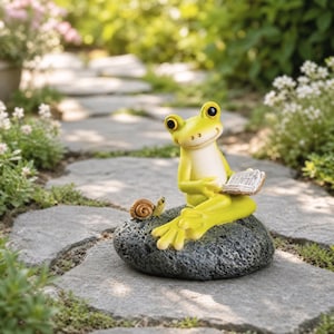 Peut inclure: Une figurine de grenouille vert citron avec un ventre crème assise sur un rocher gris foncé texturé. La grenouille tient un petit livre ouvert avec des pages visibles, et un minuscule escargot brun est posé sur le rocher près des pieds.