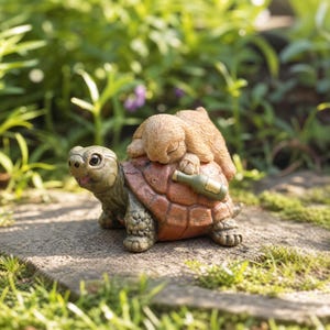 May include: A decorative garden figurine featuring a green turtle with a textured shell carrying a small, sleeping tan rabbit on its back. A miniature green glass bottle is tucked against the side of the turtle's shell, resting near the rabbit.