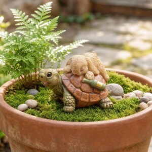 May include: A decorative garden figurine featuring a brown turtle with a small tan rabbit resting on its shell. The turtle shell has a green bottle attached to the side. The figurine is placed in a terracotta pot filled with green moss and small stones.