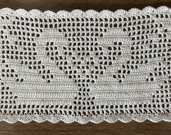 May include: A rectangular white crochet doily featuring a central heart motif created with openwork stitches. The piece has a scalloped edge border and a grid-like pattern throughout the body, showcasing intricate needlework and fine thread construction.