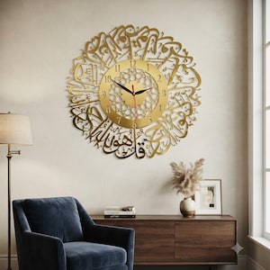 May include: A circular gold wall clock featuring intricate Arabic calligraphy surrounding a central dial with black hour and minute hands, a red second hand, and standard Arabic numerals from one to twelve arranged in a circular pattern.