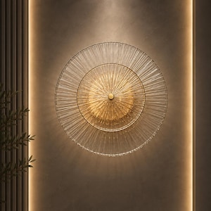 Peut inclure: Une applique murale circulaire composée de deux anneaux concentriques de tiges de verre transparentes et fines rayonnant à partir d'un moyeu central en métal doré. Le design crée un effet rayon de soleil avec un éclairage chaud diffusé.