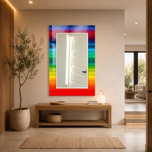 May include: A rectangular wall mirror featuring a vibrant, multi-colored border with horizontal stripes in shades of red, orange, yellow, green, blue, and purple. The central reflective glass surface shows a reflection of a white interior door.