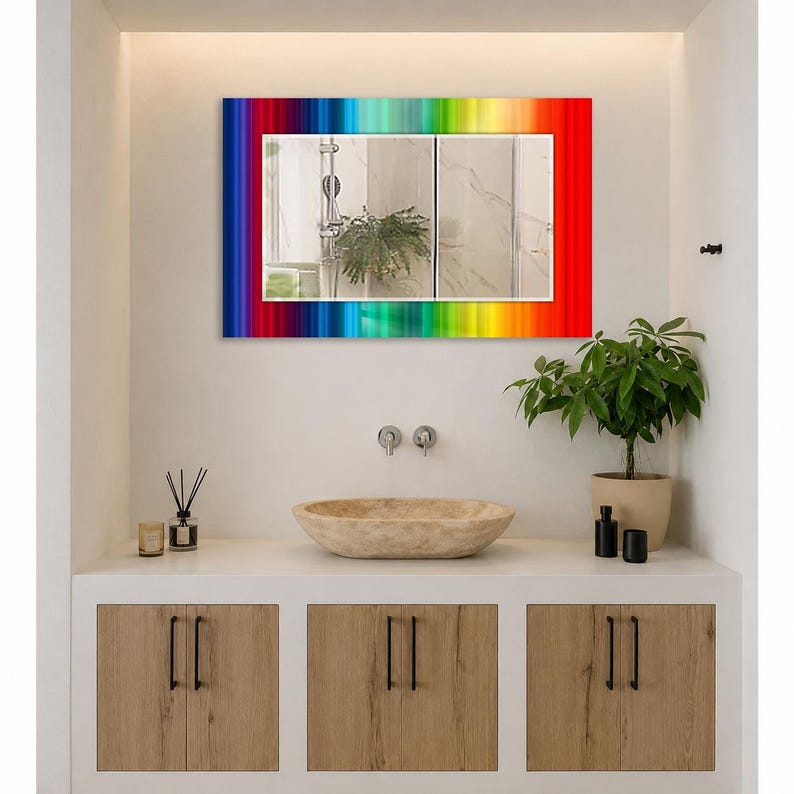 May include: A rectangular wall mirror featuring a vibrant, multi-colored rainbow border with vertical stripes in shades of red, orange, yellow, green, blue, and purple. The mirror surface reflects a bathroom interior with a plant and fixtures.