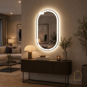 May include: An oval wall mirror with an integrated LED light strip framing the glass. The mirror is mounted above a dark brown, ribbed console table. The light emits a soft, warm glow, illuminating the wall and the surrounding space.