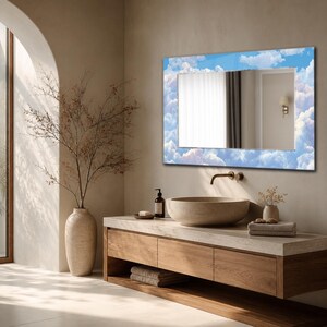 May include: A rectangular wall mirror featuring a decorative border printed with a blue sky and white clouds pattern. The mirror is mounted above a wooden vanity cabinet with a stone basin sink and a metal faucet, reflecting a room interior.