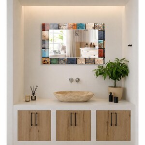 May include: A rectangular wall mirror featuring a frame composed of numerous small, square tiles in a variety of colors including blue, orange, white, brown, and gray. The mirror surface reflects a room with a window and a white cabinet.