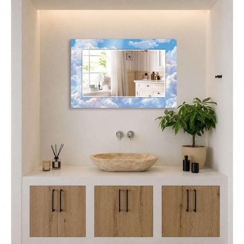 May include: A rectangular wall mirror featuring a decorative border printed with a blue sky and white clouds pattern. The mirror is mounted above a bathroom vanity, reflecting a window, white curtains, and a white cabinet with toiletries.